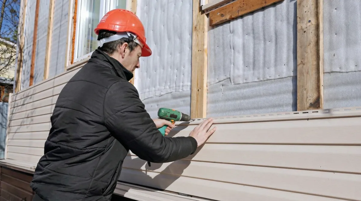 Siding replacement professional using a power drill to install new tan vinyl siding on a home exterior in Aurora, IL